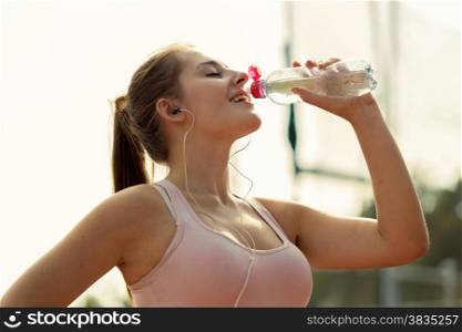 Toned photo of beautiful woman drinking water after running at hot day