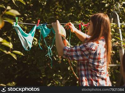 Toned photo of beautiful woman drying swimsuits on clothesline