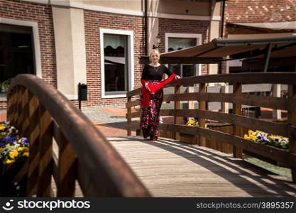 Toned photo of beautiful woman in vintage dress walking over old wooden bridge