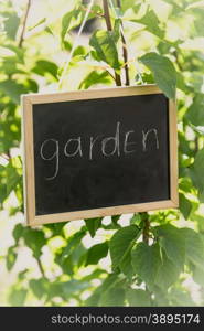 "Toned photo of blackboard with text "Garden" hanging on tree branch"