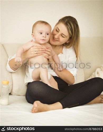 Toned photo of cheerful young mother posing with her 6 month baby on bed