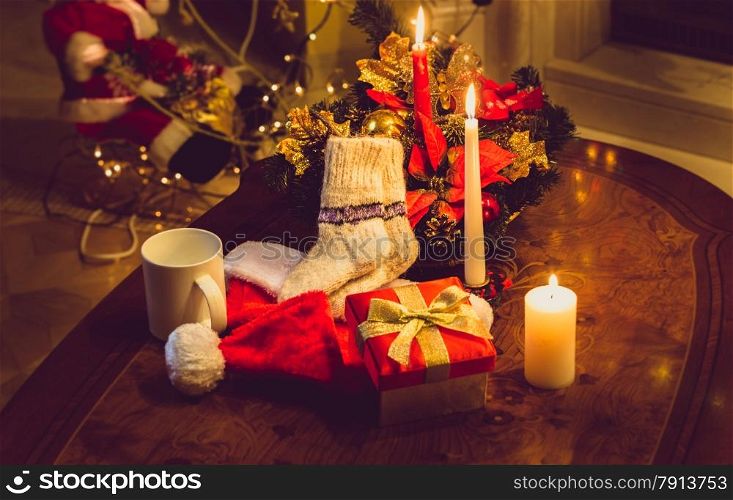 Toned photo of christmas candles, open giftbox and woolen socks on wooden table at fireplace