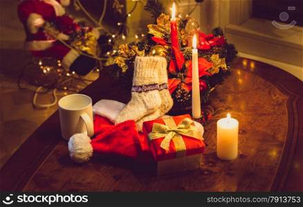Toned photo of christmas candles, open giftbox and woolen socks on wooden table at fireplace