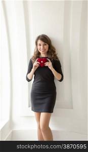 Toned photo of cute smiling girl posing with red heart at white interior