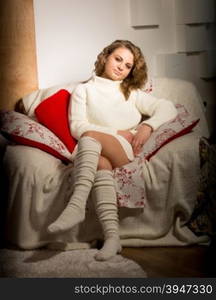 Toned photo of cute woman in sweater sitting in big armchair at living room