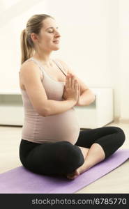 Toned photo of pregnant woman doing yoga on fitness mat at home