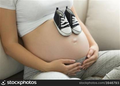 Toned photo of pregnant woman posing with baby boots on belly