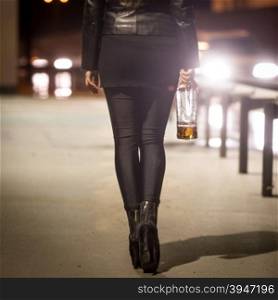 Toned photo of sexy girl with bottle walking by the road at night