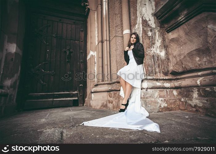 Toned photo of sexy woman in long white dress leaning against ancient wall of abbey