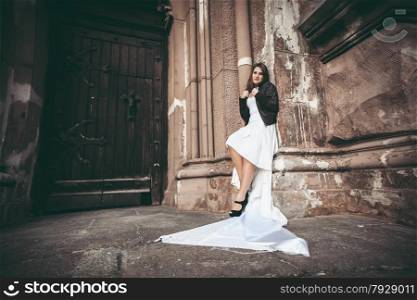 Toned photo of sexy woman in long white dress leaning against ancient wall of abbey