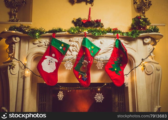 Toned photo of three red Christmas socks hanging on fireplace at house