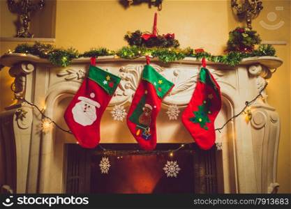 Toned photo of three red Christmas socks hanging on fireplace at house