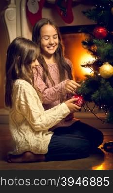 Toned photo of two cute girls sitting on floor and decorating Christmas tree
