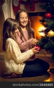 Toned photo of two cute girls sitting on floor and decorating Christmas tree