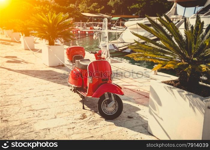 Toned photo of vintage red scooter parked on street at sunny day