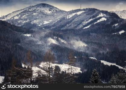 Toned photo of wind blowing on top of snowy mountains with forest