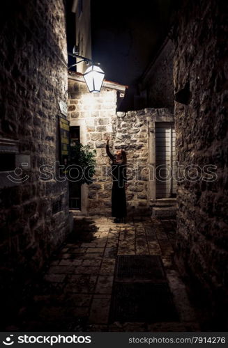 Toned photo of woman walking on narrow street lit by gas lantern