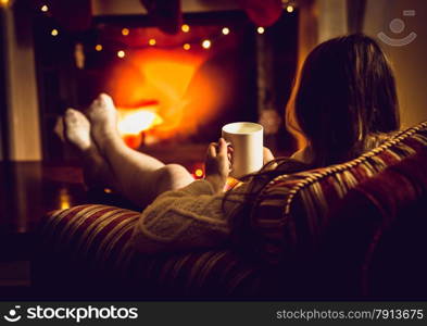 Toned photo of woman warming up with hot tea at fireplace at winter