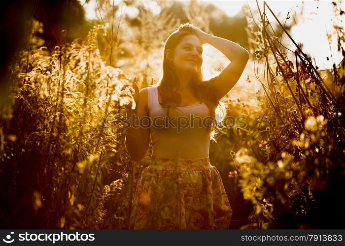 Toned photo of young brunette woman with long hair posing at field at early morning