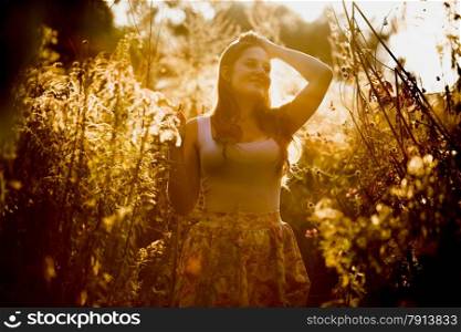 Toned photo of young brunette woman with long hair posing at field at early morning