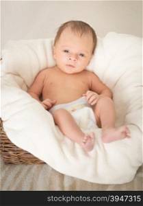 Toned portrait of 2 month old baby boy sitting in basket covered by blanket
