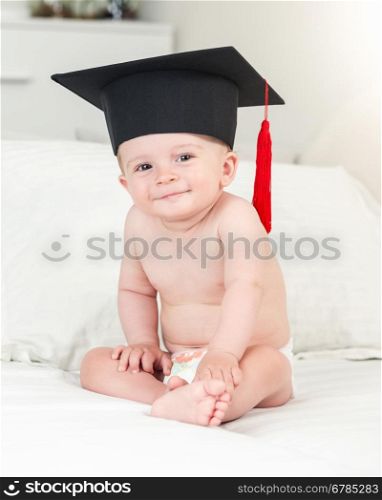 Toned portrait of adorable smiling baby boy in graduation hat looking in camera
