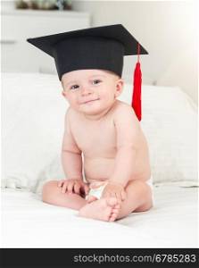 Toned portrait of adorable smiling baby boy in graduation hat looking in camera
