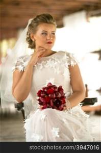 Toned portrait of beautiful elegant bride with red bouquet siting on chair