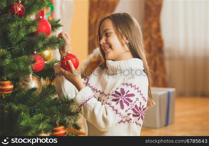 Toned portrait of beautiful girl in sweater decorating Christmas tree