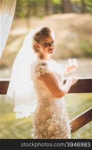 Toned portrait of beautiful young bride posing at river with glass of champagne