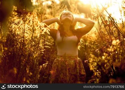 Toned portrait of beautiful young woman walking at golden field in sun rays