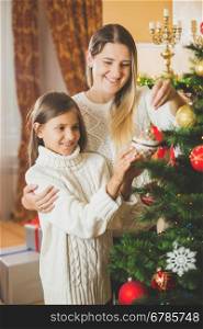 Toned portrait of cheerful young mother decorating Christmas tree with daughter at house