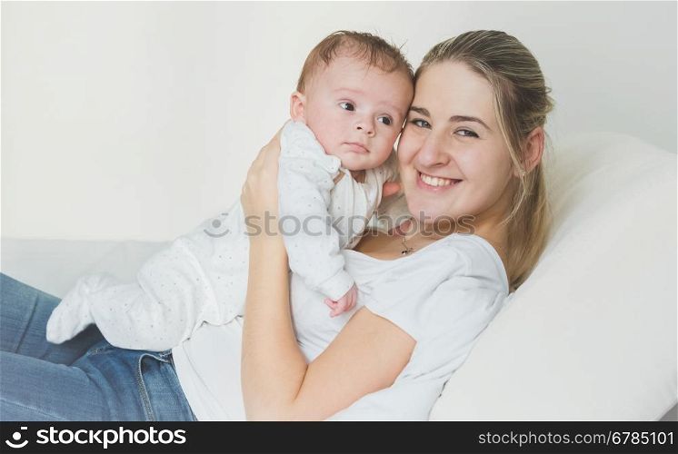 Toned portrait of cheerful young mother lying with her baby on bed