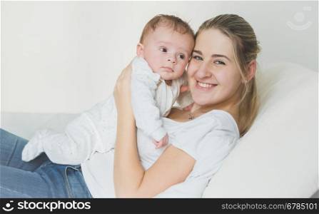 Toned portrait of cheerful young mother lying with her baby on bed