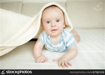 Toned portrait of cute baby boy lying on bed under the blanket