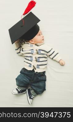 Toned portrait of cute baby boy posing in black graduation cap