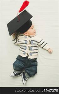 Toned portrait of cute baby boy posing in black graduation cap