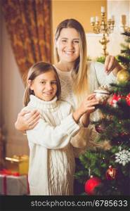 Toned portrait of cute smiling girl helping mother decorating Christmas tree
