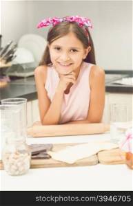 Toned portrait of cute smiling girl posing on kitchen while making dough