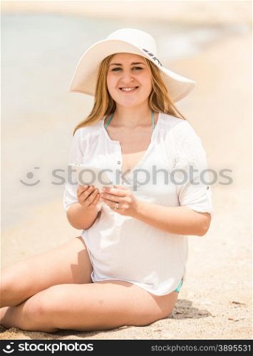 Toned portrait of cute smiling woman using digital tablet on seashore