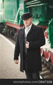 Toned portrait of handsome man in suit and bowler hat waiting for train