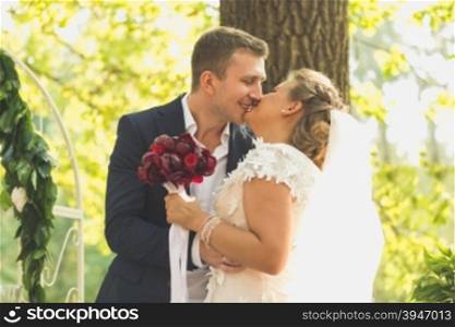 Toned portrait of happy bride and groom kissing at garden at wedding ceremony