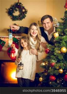 Toned portrait of happy family posing with lanterns at Christmas tree