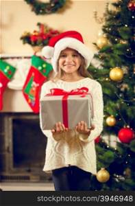 Toned portrait of happy girl in santa cap posing with Christmas gift box
