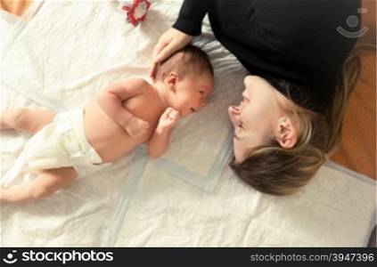 Toned portrait of happy mother lying with her newborn on bed