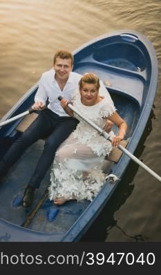 Toned portrait of happy newly married couple riding on rowing boat at sunset