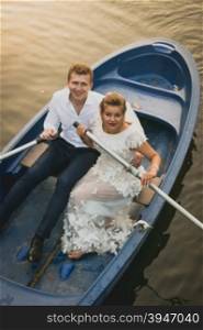Toned portrait of happy newly married couple riding on rowing boat at sunset