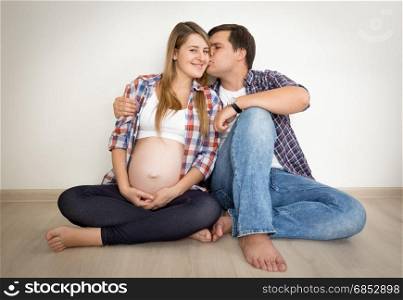 Toned portrait of happy pregnant couple sitting on floor and kissing