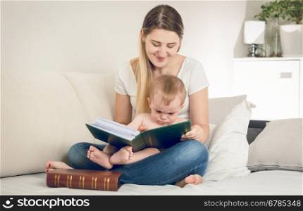 Toned portrait of happy smiling mother looking at photo album with her baby boy