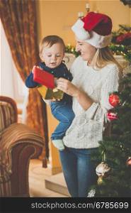 Toned portrait of happy young mother giving Christmas present to her cute baby boy at living room